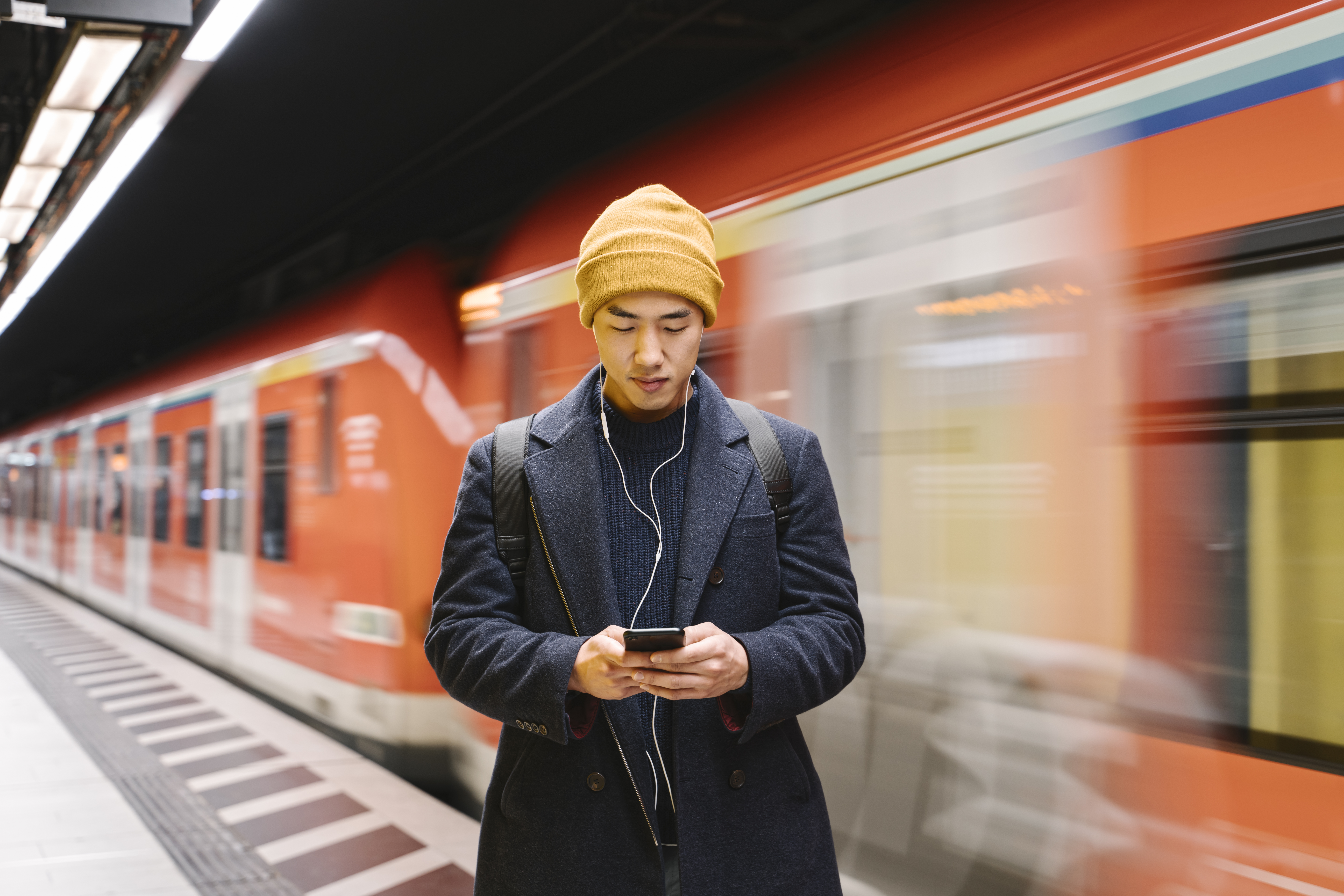 person looking at phone standing on train platform 
